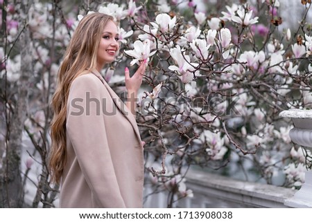 Beautiful woman with magnolia on a tree. A young smiling girl enjoys the blossoming of trees. Summertime.