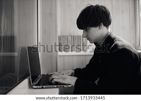 A young guy works at home on a laptop. Young attractive man sitting on a chair at home, working on a laptop. modern lifestyle at work. 
Black and white photo.
