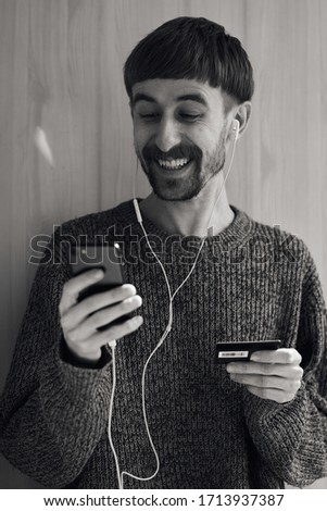 Online banking. Online shopping. A young guy in a gray sweater makes an online purchase using his phone and credit card.  Credit card and mobile phone closeup photo. Black and white photo.
