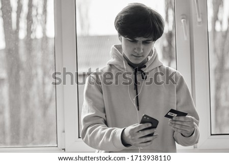 Online banking. Online shopping. A young guy  makes an online purchase using his phone and credit card. Close-up photo. Black and white photo.