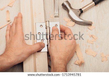 Installing the door hinge on the door frame using a hand tool, close-up, top view. Royalty-Free Stock Photo #1713945781
