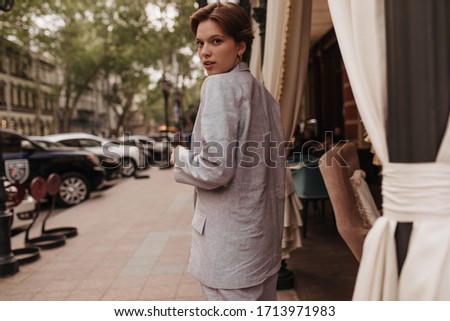 Attractive woman in grey suit walking around city. Young short-haired girl in oversize jacket and pants poses outside
