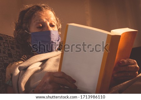Grandmother reading on the sofa reading a book (close up). Scared woman. Sick old woman with mask during coronavirus outbreak. Protection against viruses . SELECTIVE FOCUS ON WOMAN.Social distancing