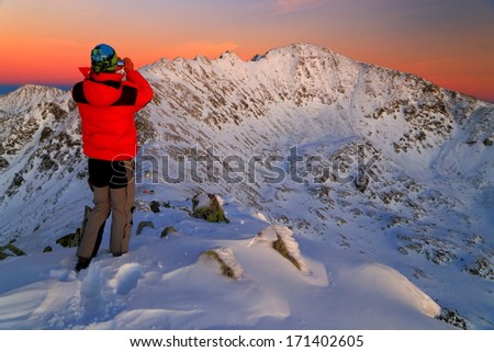 Winter mountaineer taking pictures of mountains at sunset