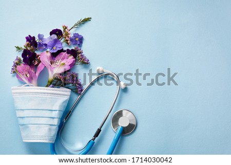 Flowers with mask and stethoscope on blue background. Happy nurse day concept. Top view Royalty-Free Stock Photo #1714030042
