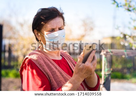 Woman in orange sweater and medical mask using her phone on empty street. Coronavirus pandemic concept.