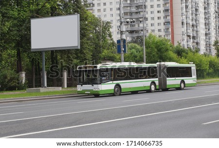Bus rides along a street in the city next to a blank white banner