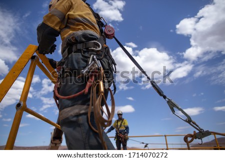 Safe workplace rigger wearing working at heights harness clipping an inertia reel shock absorbing fall arrest device hook on the rope sling anchor point while working from 2 metre exposure open edges  Royalty-Free Stock Photo #1714070272