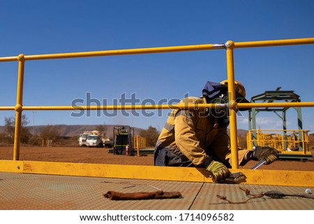 Side view of maintenance worker wearing working uniform safety fall protection helmet hand glove using vise grip and adjustable wrenches spanner when tightening bolt nut onto handrail kickboard   