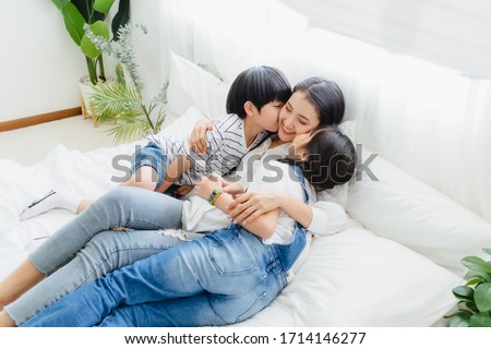 Lovely happy Asian family at cozy home. Son and daughter kiss mother with enjoy ,relax and playful together in bedroom. Happiness relationship and bonding of love between parent and children moment

