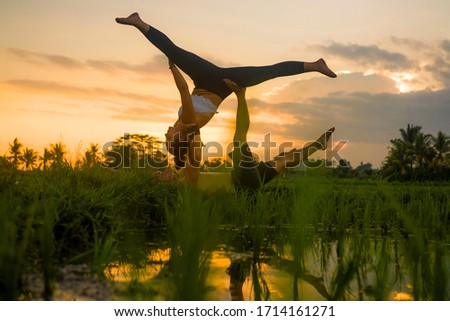 outdoors sunset acroyoga workout - young happy and fit couple practicing acro yoga drill at beautiful rice field enjoying nature and healthy lifestyle doing acrobatic pose 