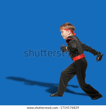 Young karate boy practicing fighting position on blue background
