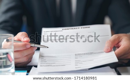 Close up of an executive hands holding a pen and contract form, indicating where to sign a contract while sitting at office desk.