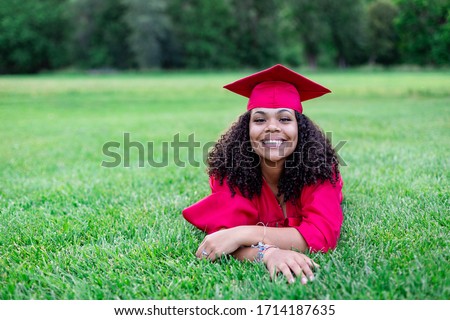 Portrait of a beautiful multiethnic woman in her graduation cap and gown. Smiling and cheerful as she poses lying down in the grass