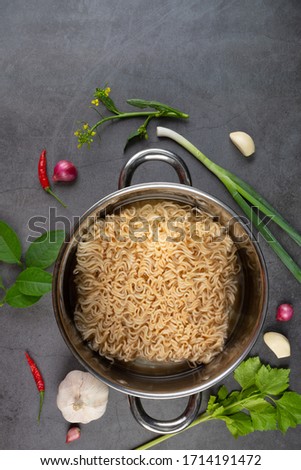 Pot of raw instant noodle with ingredients of soup on black background.