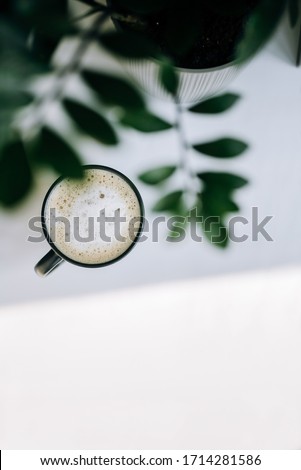 Black cup with coffee on white table with plant in the morning, vertical photo