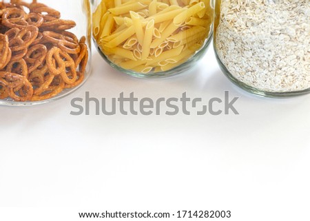 Pasta, oatmeal and pretzels in glass jars on white background on kitchen.Stocks of non-perishable products on a light background.Organized home simple stylish storage no plastic. Selective focus