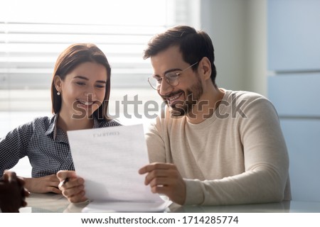 Young successful couple, man and woman reading business document at mortgage negotiating. Happy smiling husband in glasses and wife making deal together in broker office. Royalty-Free Stock Photo #1714285774