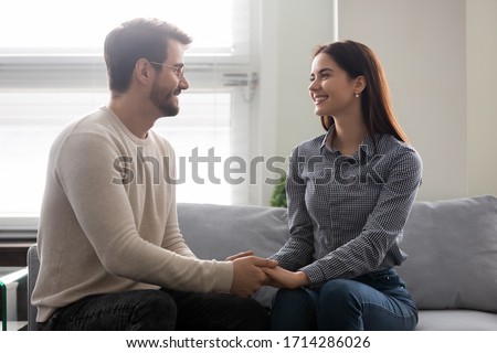 Happy young man holding attractive woman hands on couch. Smiling romantic couple enjoy time together. Beautiful family have fun time and enjoy romantic pastime. Royalty-Free Stock Photo #1714286026
