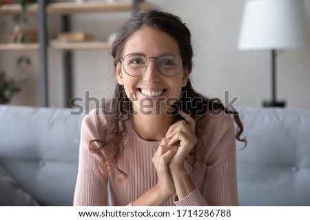 Head shot close up beautiful smiling young woman in eyewear looking at camera, holding video job interview from home. Web cam view happy smart female blogger recording vlog alone in living room. Royalty-Free Stock Photo #1714286788