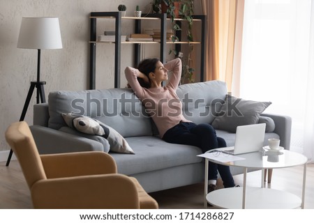 Full length carefree young attractive caucasian woman resting on sofa with closed eyes. Calm millennial female freelancer businesswoman enjoying break pause time, working from home online on computer. Royalty-Free Stock Photo #1714286827