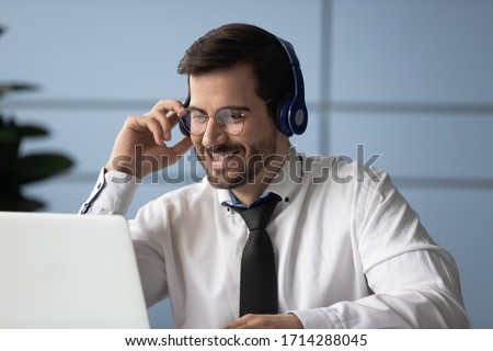 Happy businessman listening using headphones looking at laptop screen. Smiling man operator working in call center and support people. Manager communicating with client.