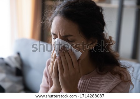 Close up head shot unhealthy young lady using paper tissue, wiping runny nose. Unhappy stressed woman suffering from seasonal allergy or caught cold, blowing nose or coughing in handkerchief. Royalty-Free Stock Photo #1714288087