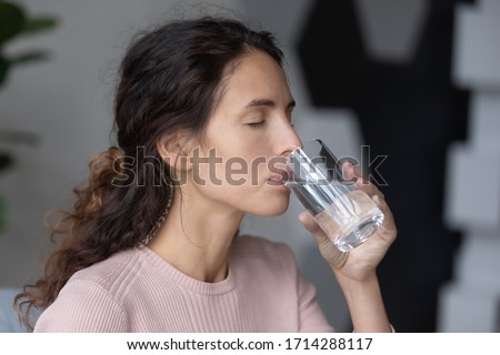 Side head shot close up view peaceful calm attractive millennial woman drinking glass of pure distilled aqua. Happy young lady enjoying everyday habit, sipping clear water in morning at home. Royalty-Free Stock Photo #1714288117