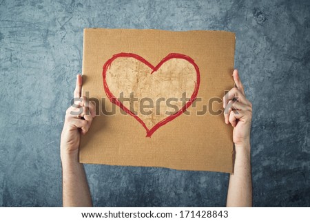 Man holding cardboard paper with heart shape drawing as Valentines day conceptual image.