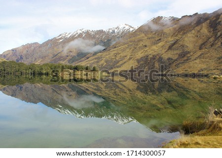Reflections of Moke Lake, Otago, New Zealand. Still water, backed by snow capped mountains and grassy plains.  