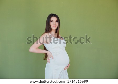Picture of happy pregnant woman posing isolated over green wall. Looking at camera and smiling.