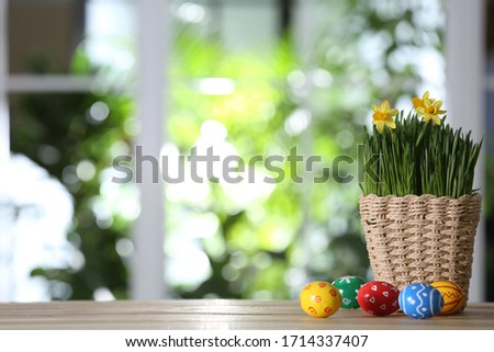 Colorful Easter eggs and flowers on wooden table against blurred green background. Space for text