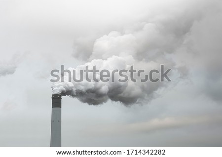 Thick and heavy smoke coming out of a huge and high chemical factory chimney under a misty and rainy sky Royalty-Free Stock Photo #1714342282