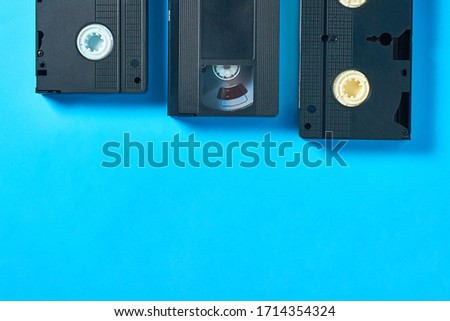 Row of three black old plastic vhs video cassettes near blank notepad lies on blue desk. Concept of 90s. Copy space. Top view
