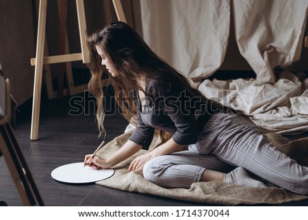 Brunette girl sitting on the floor draws with a brush