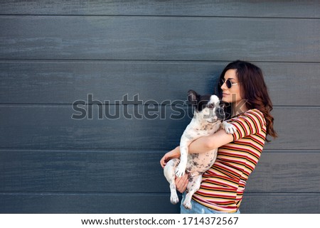Young attractive woman holding french bulldog  dog in hands. Cute and glamorous girl in trendy sunglasses posing with dog. Beautiful young girl holding cute dog