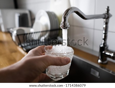 potable water and safe to drink. man filling a glass of water from a stainless steel kitchen tap. male's hand pouring water into the glass from chrome faucet to drink running water with air bubbles. Royalty-Free Stock Photo #1714386079