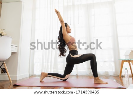 A beautiful Asian woman's fitness at home instead of going to the gym. She is practicing Crescent Lunge on the yoga mat. She wears sportswear. Exercise concept for good shape Royalty-Free Stock Photo #1714390435
