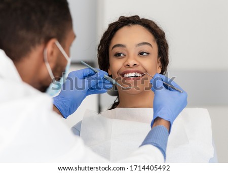 Pretty black lady in dentist chair looking at her doctor with smile, close up Royalty-Free Stock Photo #1714405492