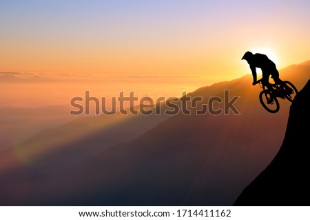 Silhouette of a mountain biker enjoying downhill during the sunset. Cyclist silhouette on the hill beautiful colorful sky and clouds in the background. Royalty-Free Stock Photo #1714411162