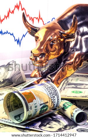 Concept of exchange trading in bull market.  Brass bull near rolled one hundred us dollar bill. Stock market prices chart in background.