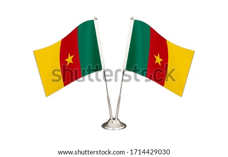 Cameroon table flag isolated on white ground. Two flag poles with flags and Cameroon flag on the table.