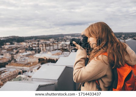 Beautiful female photographer taking pictures of old town. Tourist or female traveller have professional camera. Alone on top of tower. Urban view.