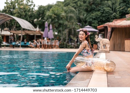 Young asian woman relax on summer holiday traveller concept. Beautiful girl with flower bikini and donut inflatable beside pool at Pattaya, Bangkok. Background with copy space.