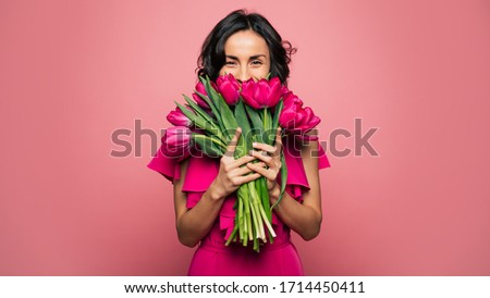 International Women's Day. Extremely happy woman in a bright pink dress is smelling a bunch of spring flowers, which she is holding in her hands. Royalty-Free Stock Photo #1714450411