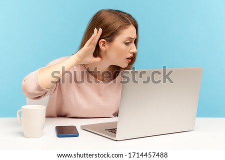 I can't hear, Woman holding arm near ear trying to listen secret talk on video call on laptop, bad internet connection, online conference from home office. indoor studio shot isolated, blue background Royalty-Free Stock Photo #1714457488