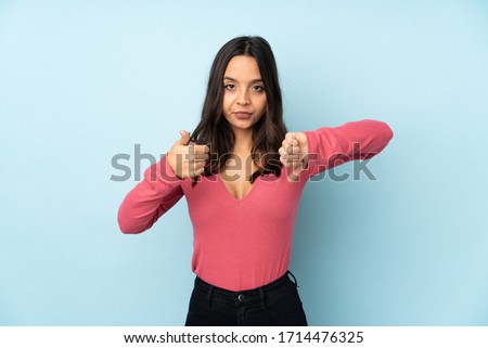 Young mixed race woman isolated on blue background making good-bad sign. Undecided between yes or not
