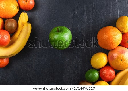 Assortment of tropical fruits orange, tangerine, banana, grapefruit, lemon, lime, kiwi on dark background. Fresh fruit set with apple. top view, copy space.