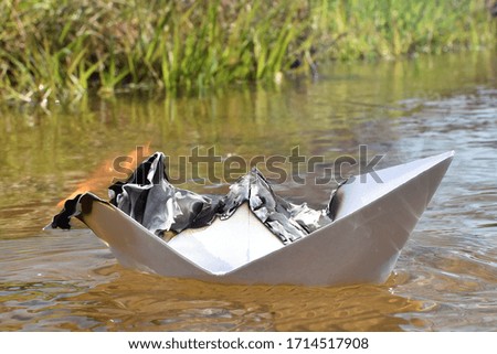 A white paper boat floats in a river while it is burning - Abstract concept with burning paper boat on the water as a symbol for sea rescue or as a contradictory representation of elements