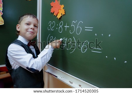 second grade student solves math example on green blackboard Royalty-Free Stock Photo #1714520305